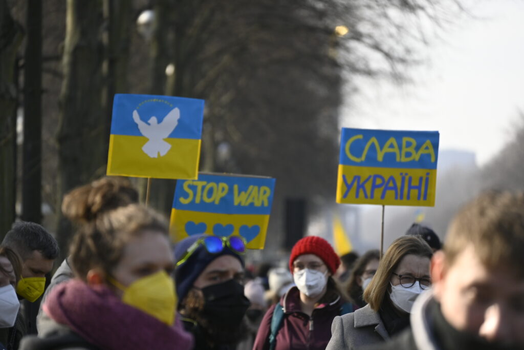 Demonstrierende in Berlin halten Schilder hoch mit mit ukrainischen Flaggen, einer Friedenstaube und Aufforderungen auf kyrillisch.